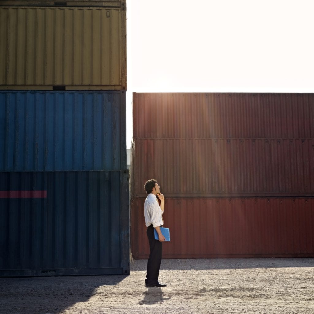 Man stands in front of shipping containers to illustrate how to build a shipping container home