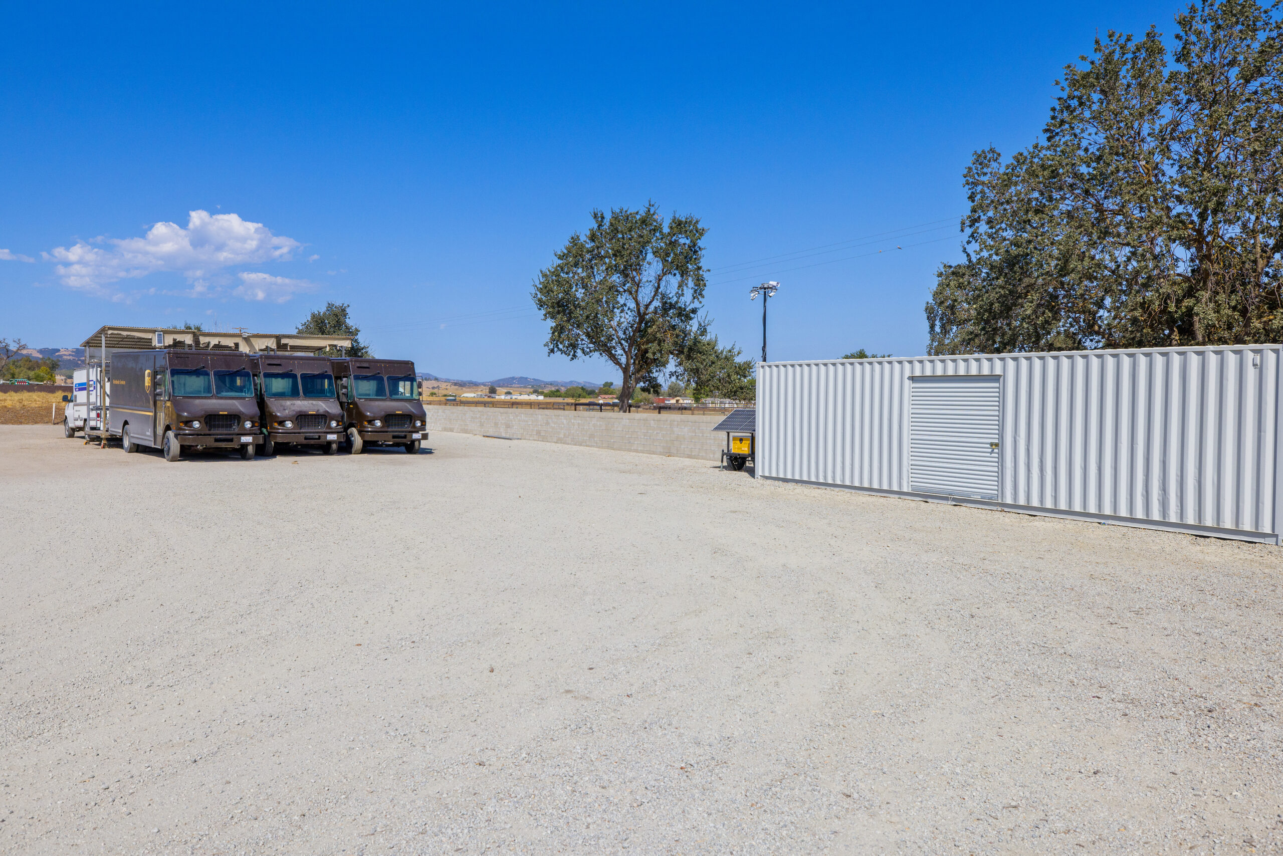 A row of delivery trucks parked next to a commercial storage container from Container Stop.